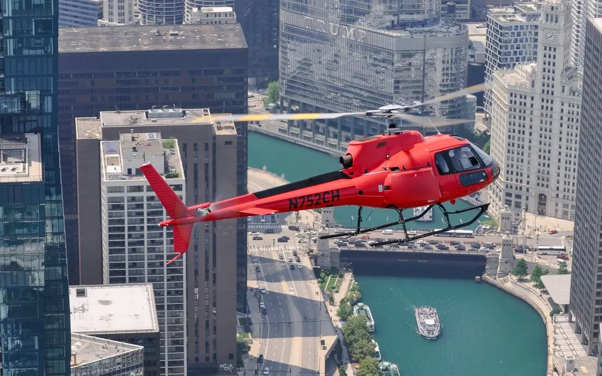 A red helicopter flying above the river between downtown towers